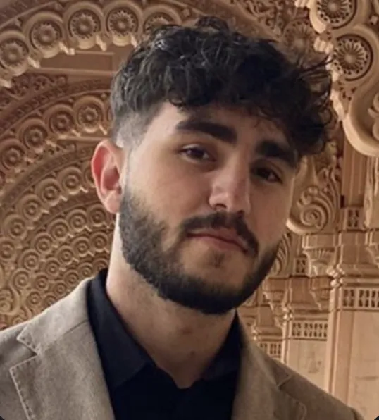 Majd Khalaf with a beard and curly hair, wearing a jacket, posing in front of an ornate architectural background.