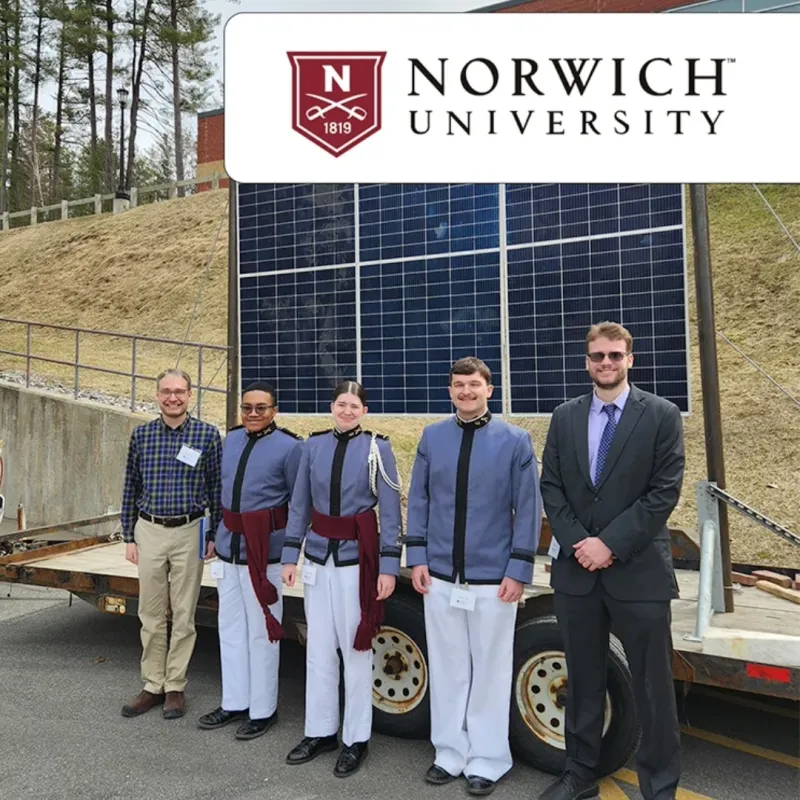 Group of five individuals standing in front of a large solar panel at Norwich University.