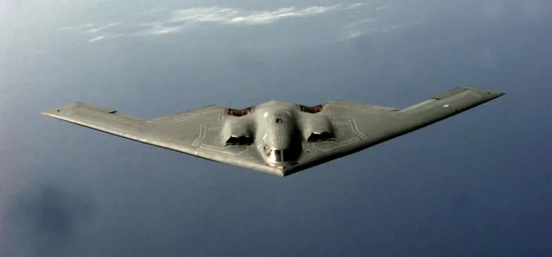 A B-2 Spirit stealth bomber in flight against a cloudy sky.