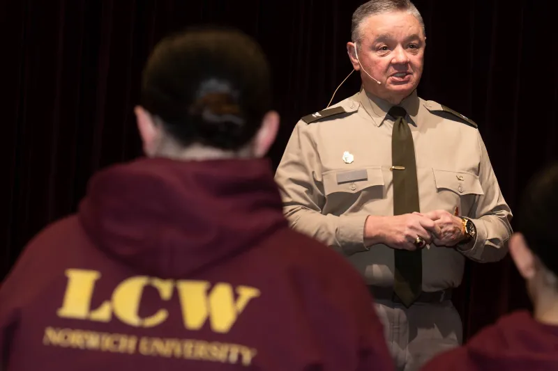 Person in uniform speaks to people wearing maroon hoodies labeled LCW Norwich University.