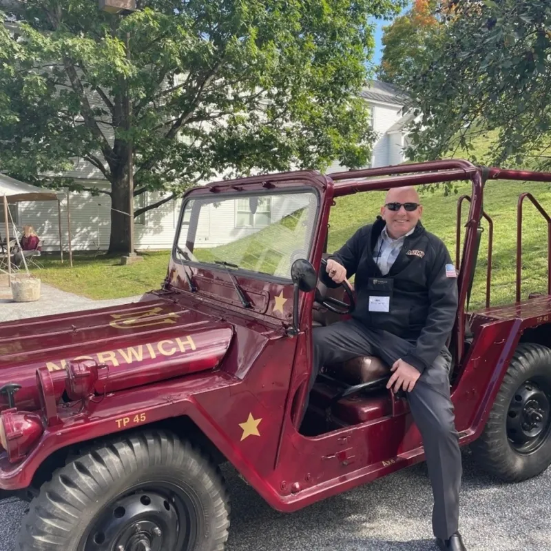 A man smiles as he sits in a custom-painted, old Norwich Jeep.