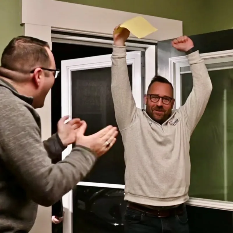 a man in foreground, facing another man with hands in air, holding a paper ballot