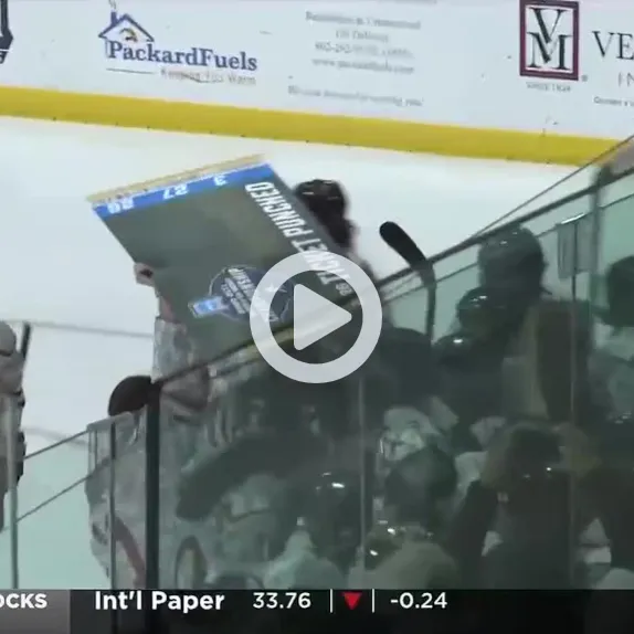 Hockey player holds a championship sign above the bench beside the rink glass.
