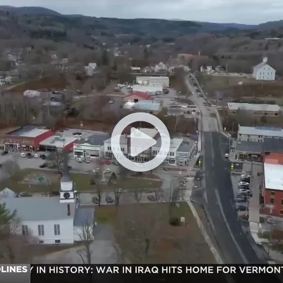 Aerial view of a small town with roads, buildings, and hills in the background.