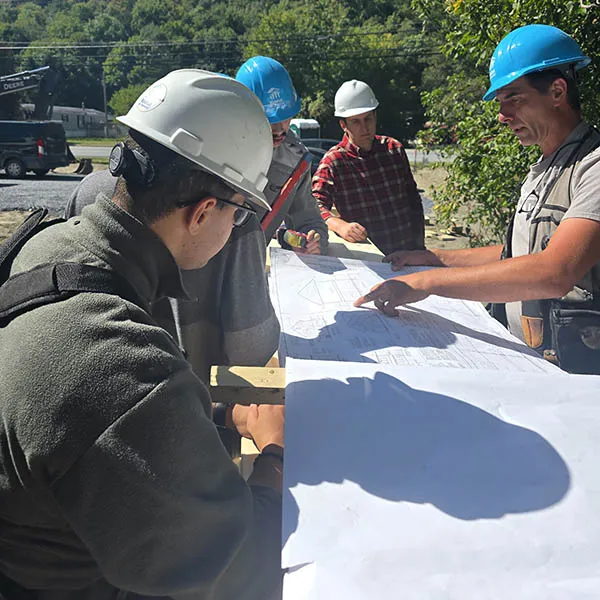 Four people in hard hats review building plans together at a construction site.