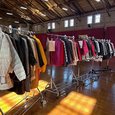Clothing hangs on several rolling racks inside a large hall.